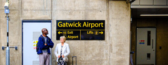 Man and woman look in opposite directions beneath a directional sign on the platform at Gatwick Airport railway station