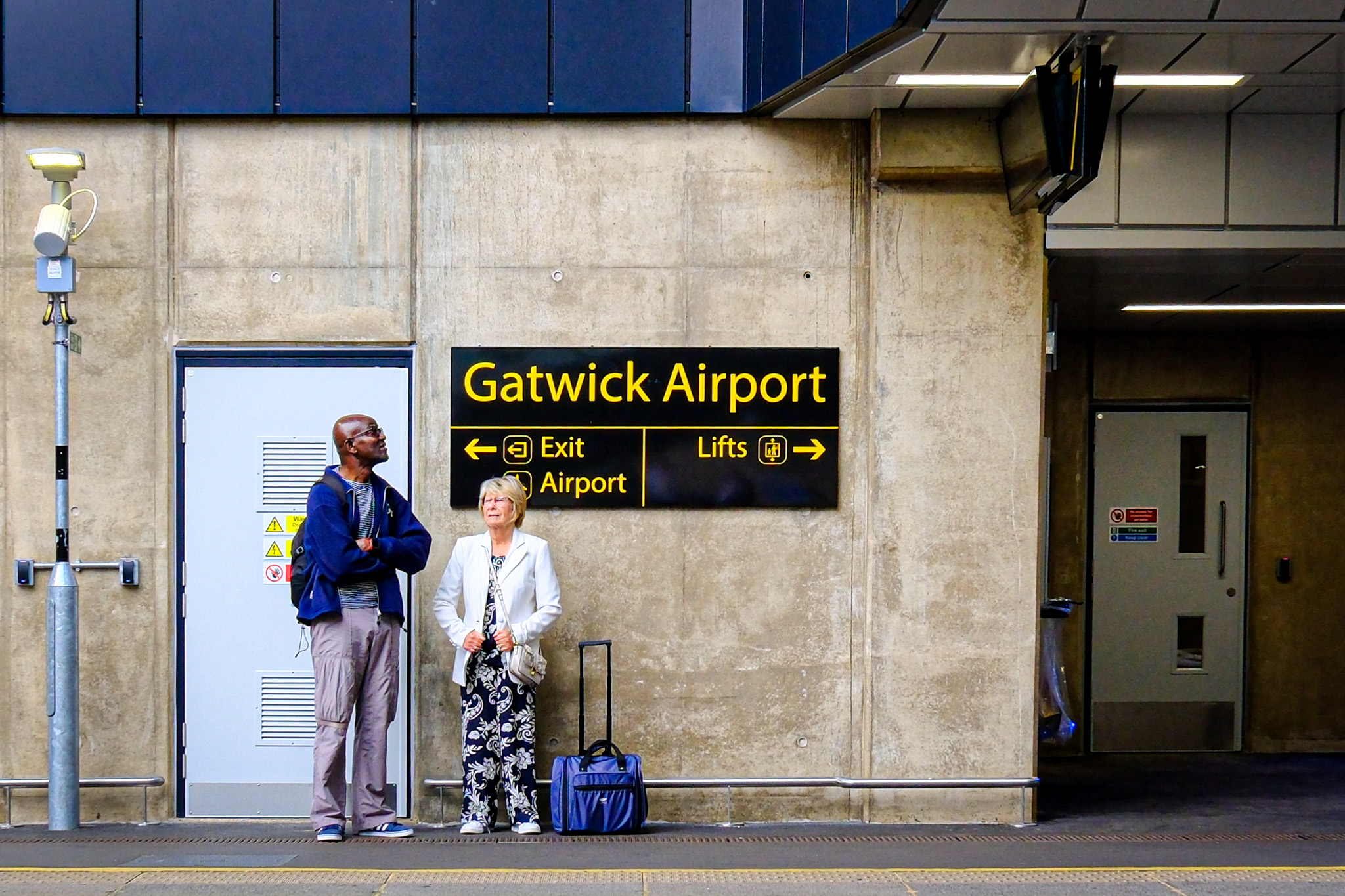 Man and woman look in opposite directions beneath a directional sign on the platform at Gatwick Airport railway station